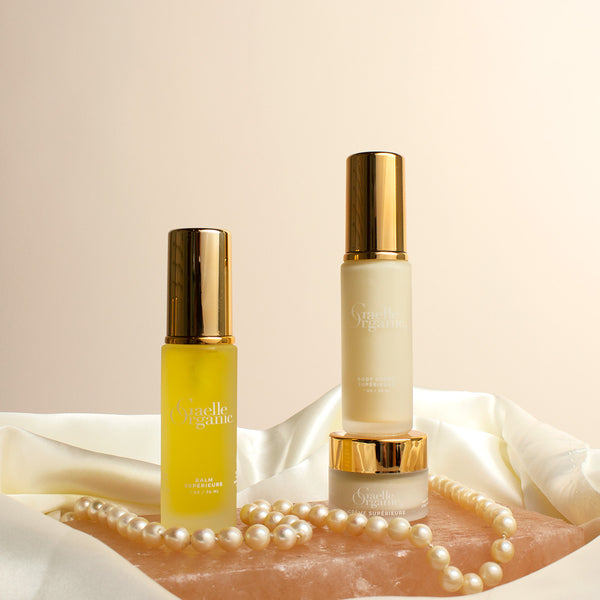 Set of travel-size organic facial and body  moisturizers for mature skin, on a pink stone with pearls and a silk scarf