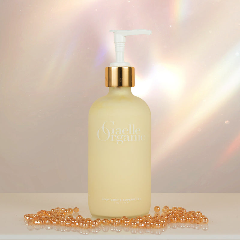 Body Creme Superieure, a hydrating organic body lotion for mature skin, on a white surface with shiny gold beads.