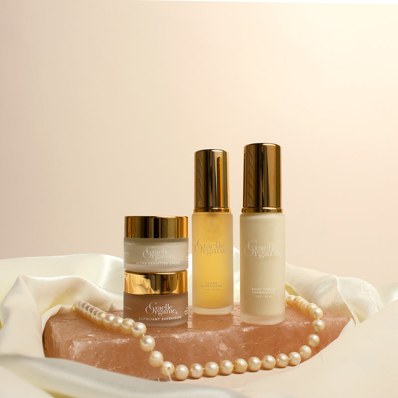 Organic anti-aging essentials -  body lotion, moisturizing exfoliator, the best moisturizer for dry sensitive skin, and an organic pore minimizer, in a convenient travel set bundle, shown with pearls on a rose quartz slab